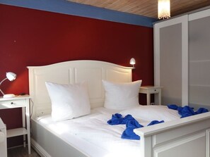Una cama con ropa de cama y almohadas blancas, una lámpara de noche y una toalla azul sobre la cama.