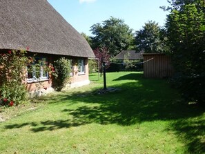 Une maison avec un toit de chaume, une pelouse bien entretenue et un abri en bois à l’arrière-plan.