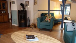 Un salon chaleureux avec une table basse ronde en bois, des fauteuils turquoise et un poêle à bois noir.