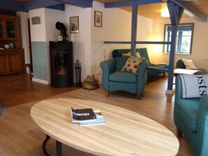 Un salon chaleureux avec une table basse ronde en bois, des fauteuils turquoise et un poêle à bois noir.