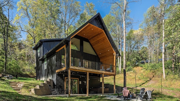 Une cabane moderne dotée d’une grande terrasse, entourée d’arbres.