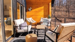 Une terrasse en bois avec des meubles d’extérieur, une porte d’entrée en verre et une vue sur les arbres.