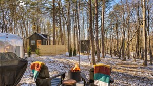 A campsite with two chairs, a fire pit, and a covered grill.