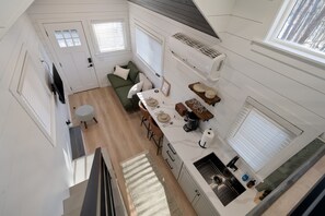 Eine kompakte, moderne Küche mit weißen Schränken, ein Essbereich mit Tisch für zwei Personen und eine kleine Sitzecke mit einer Couch.
