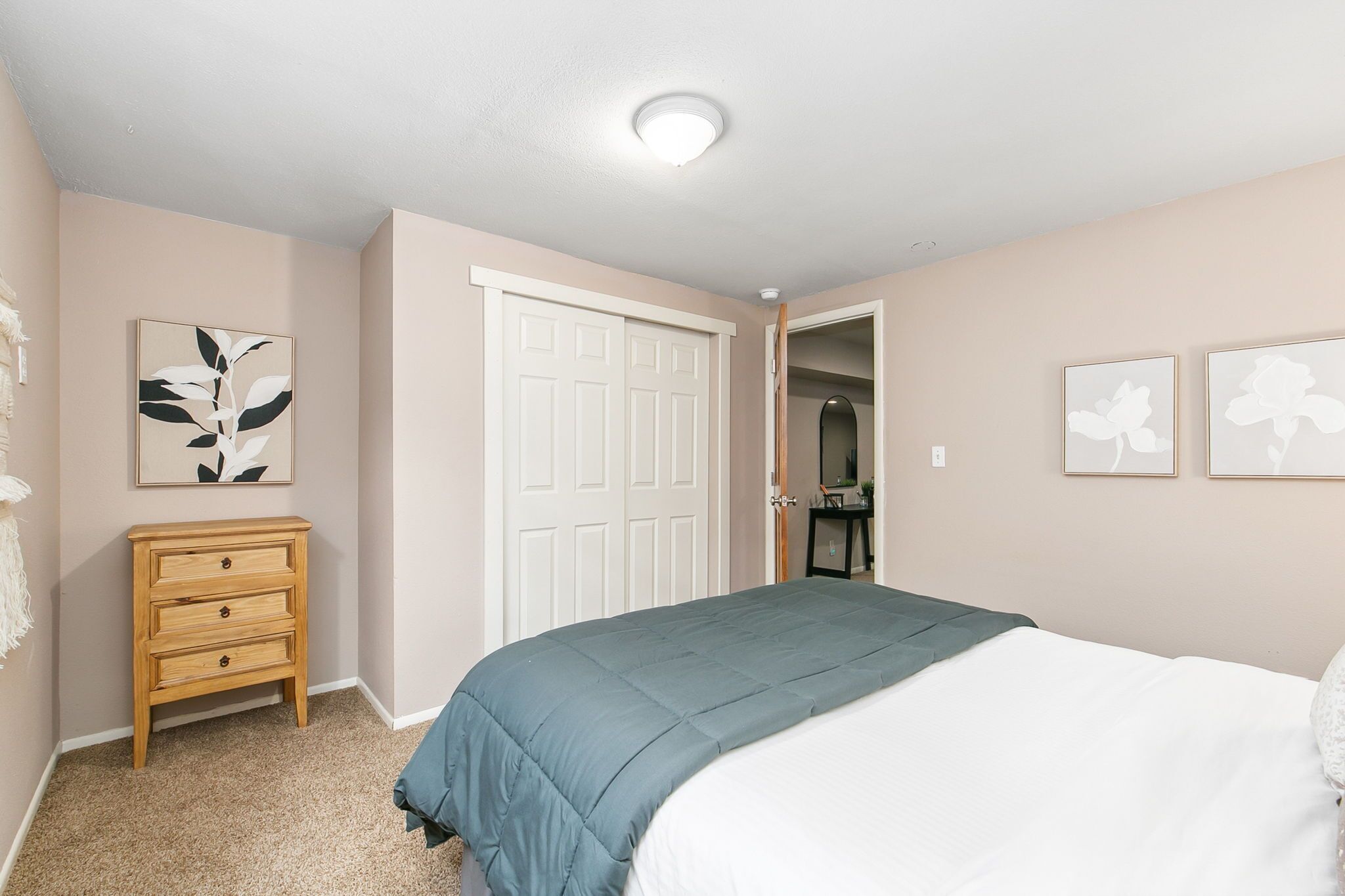 A bedroom with a bed, a dresser, a closet, and artwork on the walls.