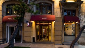 Entrada de un hotel con un toldo rojo, una puerta visible y un letrero con el nombre del hotel.