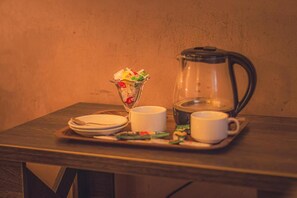 A table with a coffee pot, a glass pitcher, and a tray with plates, cups, and a bowl of snacks.