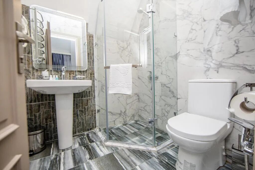 A bathroom with a marble floor, a white sink, a toilet, and a glass shower enclosure.