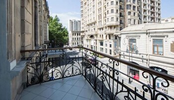 Een balkon met gedetailleerde zwarte hekwerk, uitkijkend op een straat met hoge gebouwen.