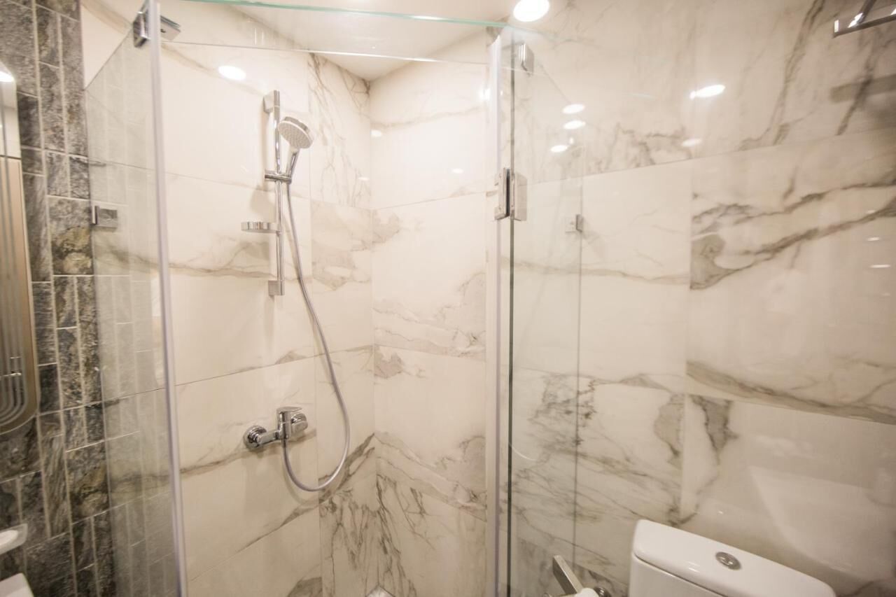 Een moderne badkamer met een douchecabine van glas, marmeren wanden en een toilet.
