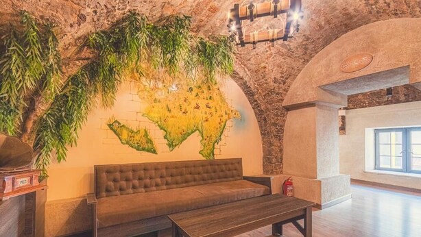 Una habitación con sofá, un banco de madera, un mural de un mapa y una pared de piedra.