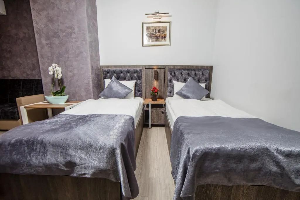 A hotel room with two beds, a nightstand with a lamp, a framed picture on the wall, and a potted orchid.