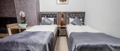 A hotel room with two beds, a nightstand with a lamp, a framed picture on the wall, and a potted orchid.