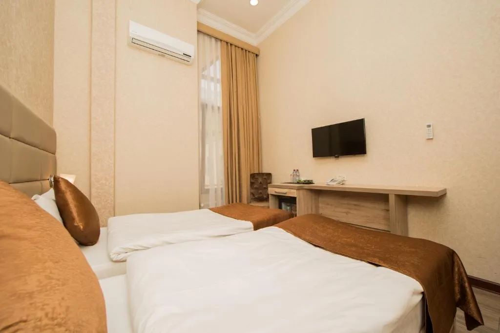 Quarto de hotel com duas camas, televisão, escrivaninha e janela com cortinas.