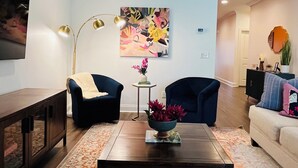 Een woonkamer met een donkere salontafel, twee fauteuils, een bank, een kamerbreed tapijt, een schilderij aan de muur en een lamp.