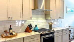 Een moderne keuken met witte kasten, een roestvrijstalen afzuigkap en een betegelde achterwand.