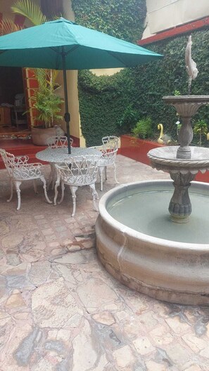 An outdoor patio with a fountain, white metal chairs, and a green umbrella. - San Cristóbal Bleisure Hotel (San Cristóbal de las Casas)
