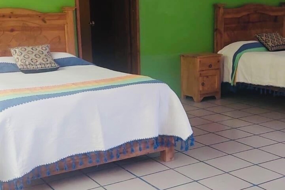 A bedroom with two beds, green walls, and tiled flooring.