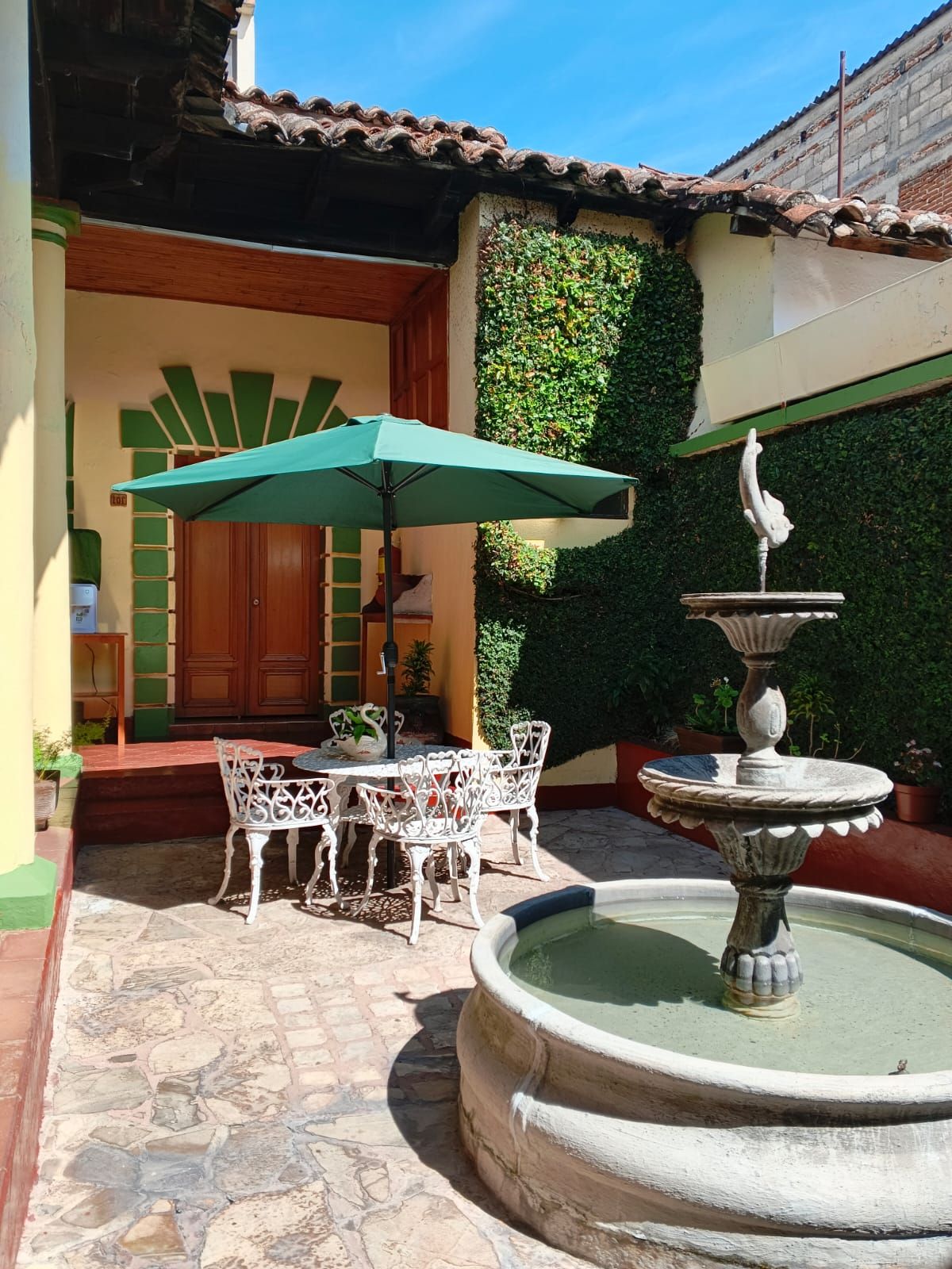 Un patio al aire libre con una mesa, sillas, una fuente y un paraguas verde.