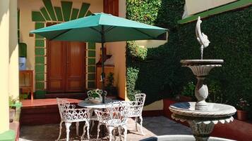 Un patio al aire libre con una mesa, sillas, una fuente y un paraguas verde.
