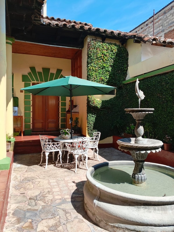 An outdoor patio with a table and chairs, a fountain, and a green umbrella.