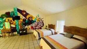 Hotellihuone, jossa on kaksi sänkyä, työpöytä, tuoli, peili ja seinällä suuri seinämaalaus.