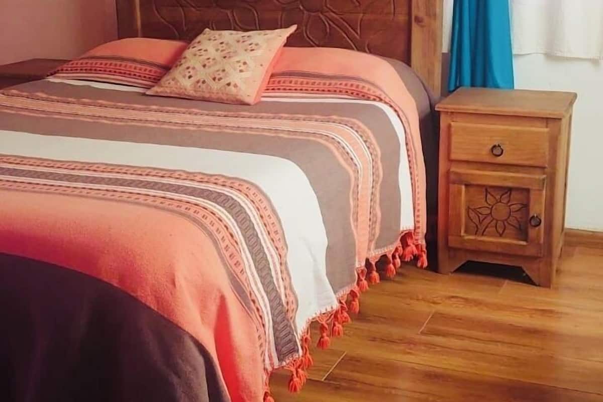 A bedroom with a wooden bed, a nightstand, and a window with blue curtains.
