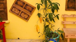 Una pared amarilla con contraventanas de madera, una planta en maceta y un pequeño banco.