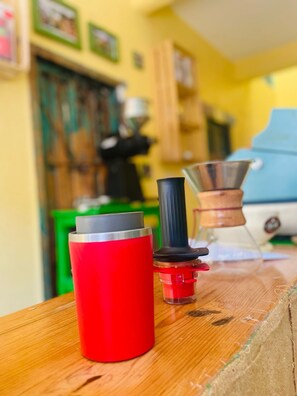 A red thermos, a metal funnel, and a wooden container on a wooden table in a kitchen with yellow walls and green cabinets. - San Cristóbal Bleisure Hotel (San Cristóbal de las Casas)