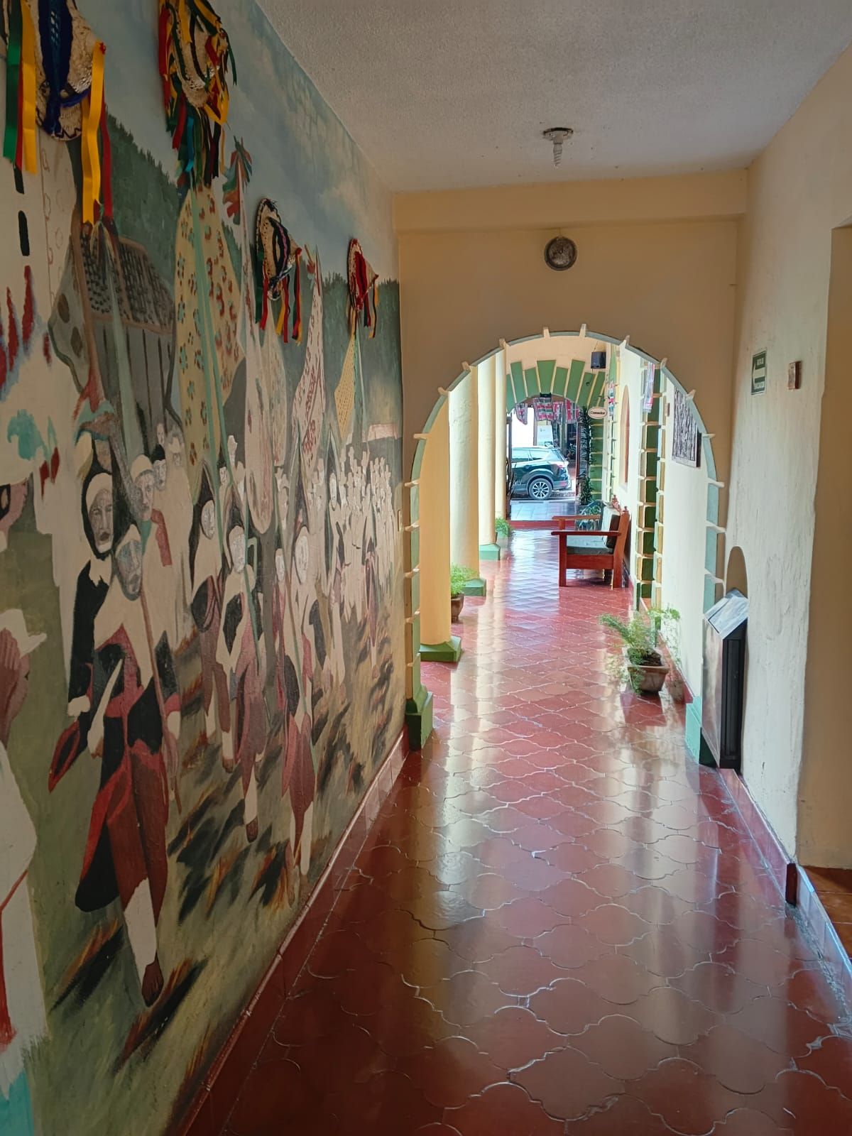 Un pasillo con un mural a la izquierda, que conduce a una habitación con un coche estacionado afuera.