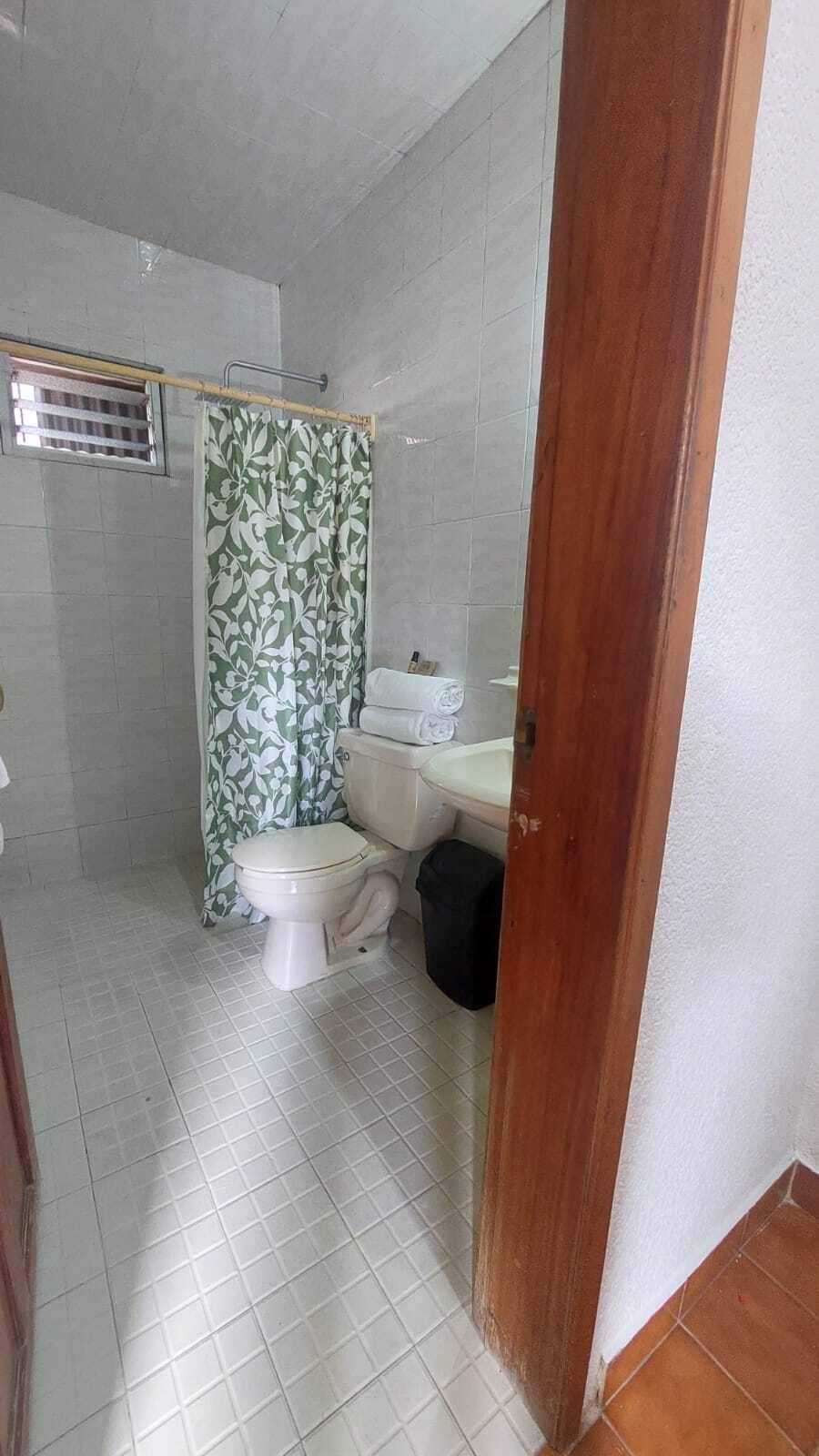 Un baño con inodoro, cortina de ducha y un cubo de basura.