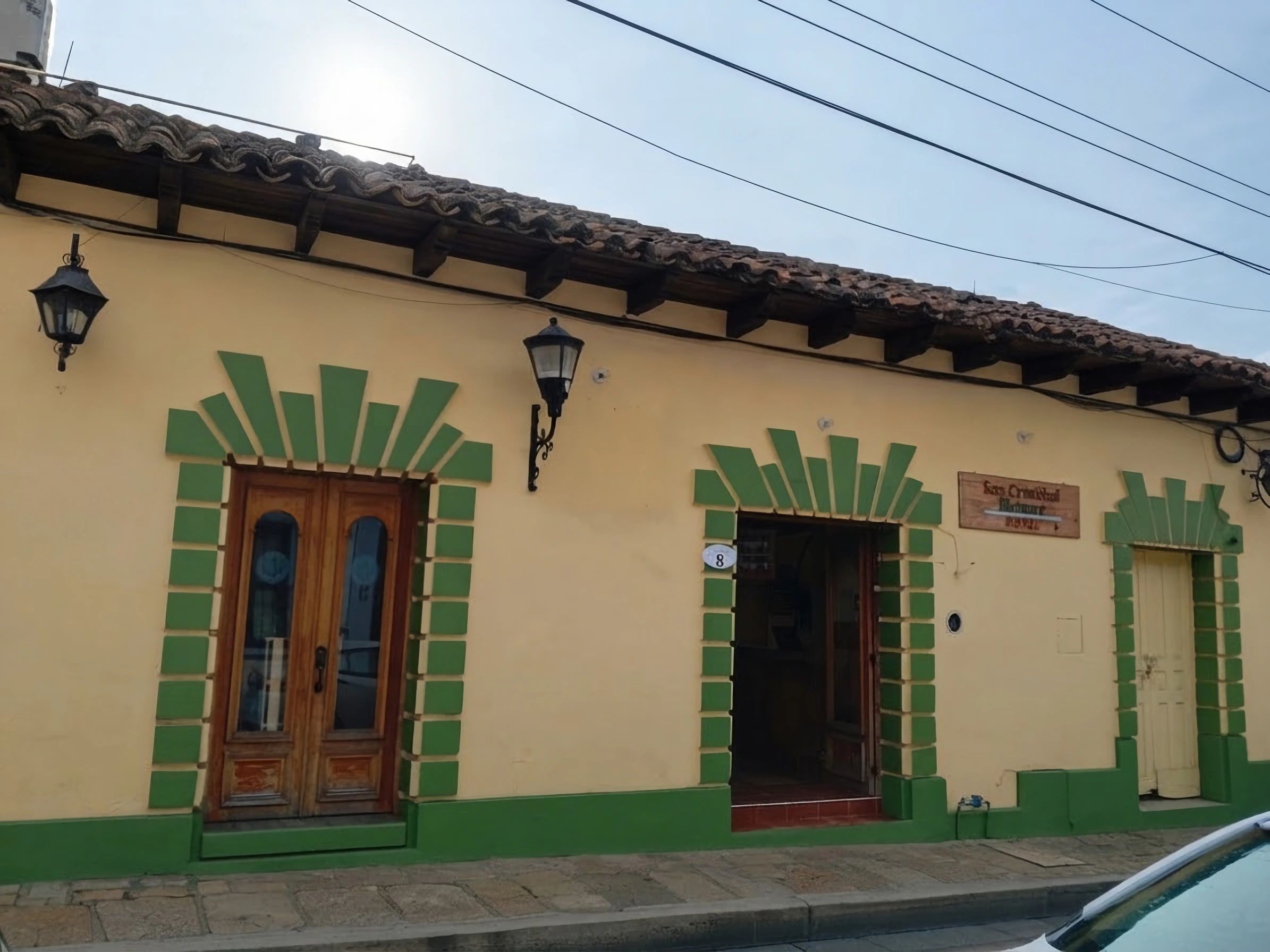 Un edificio con techo de tejas, puertas con marco verde y un letrero que indica un hotel.