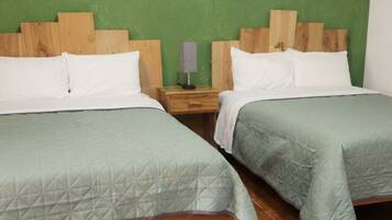 Dos camas individuales con cabeceros de madera, una mesita de noche con lámpara y una pared verde.