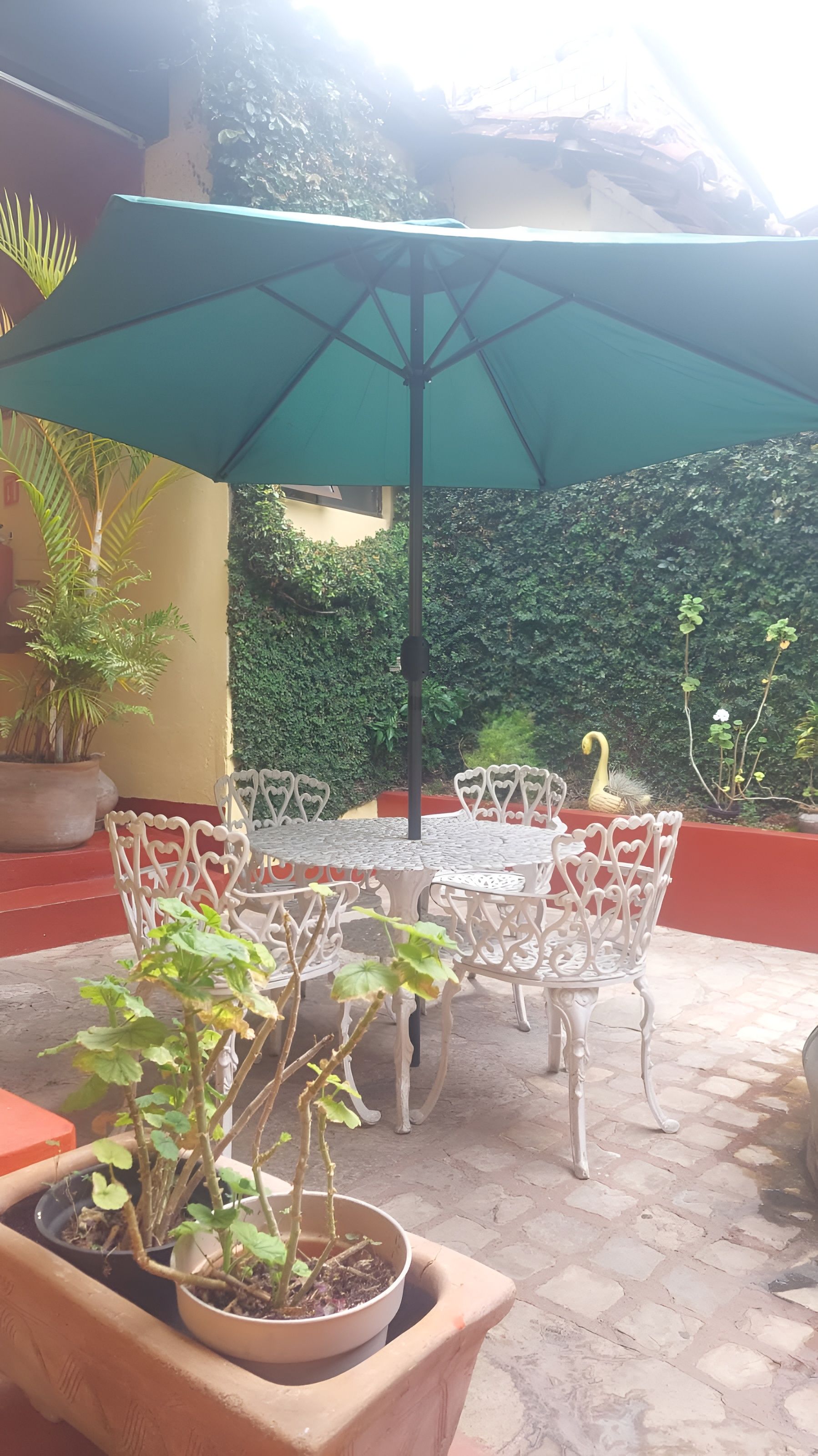 Une terrasse extérieure avec une table ronde, des chaises blanches, un parasol vert et des plantes en pot.