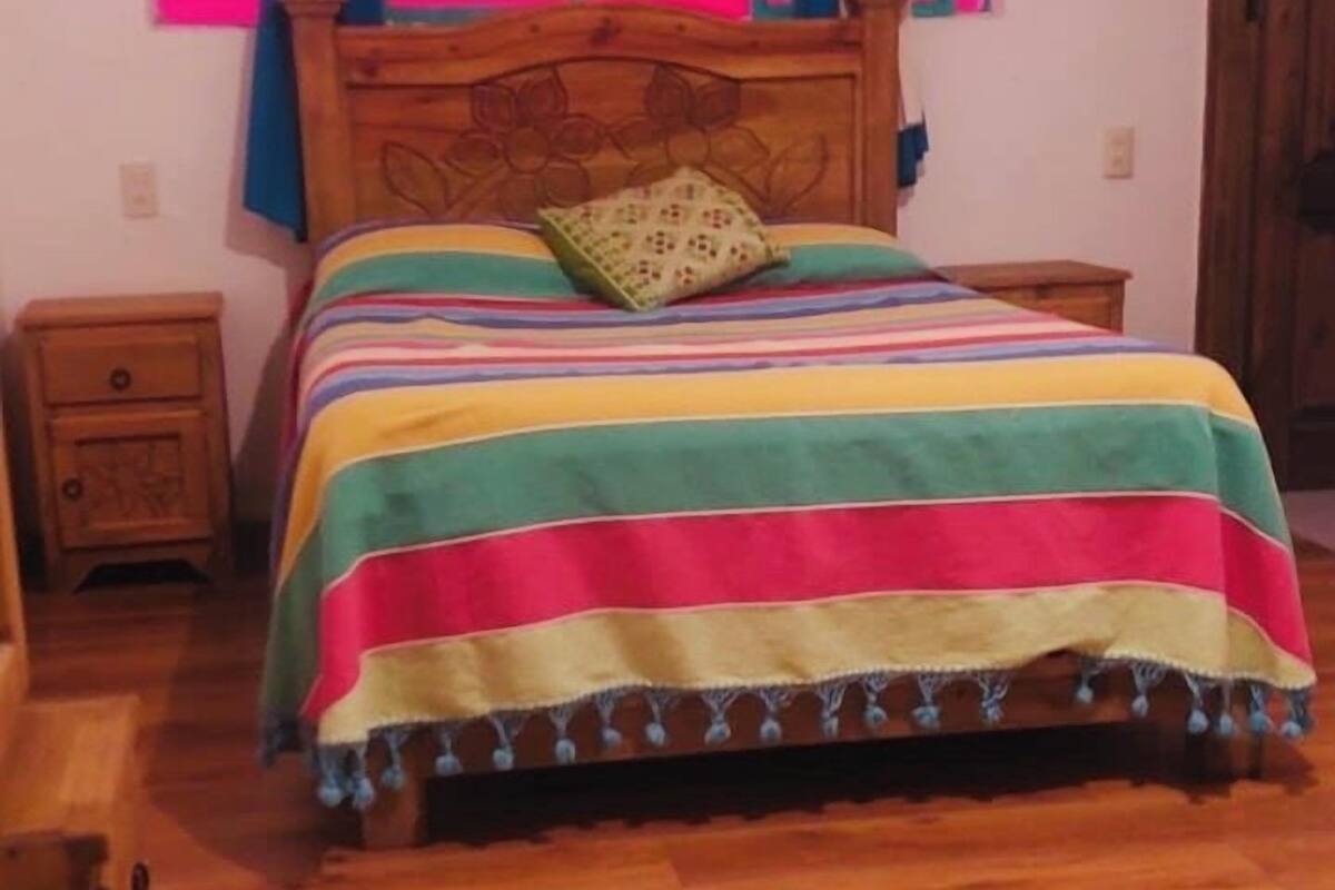A bed with a colorful striped bedspread, a wooden headboard, and a window with pink curtains.