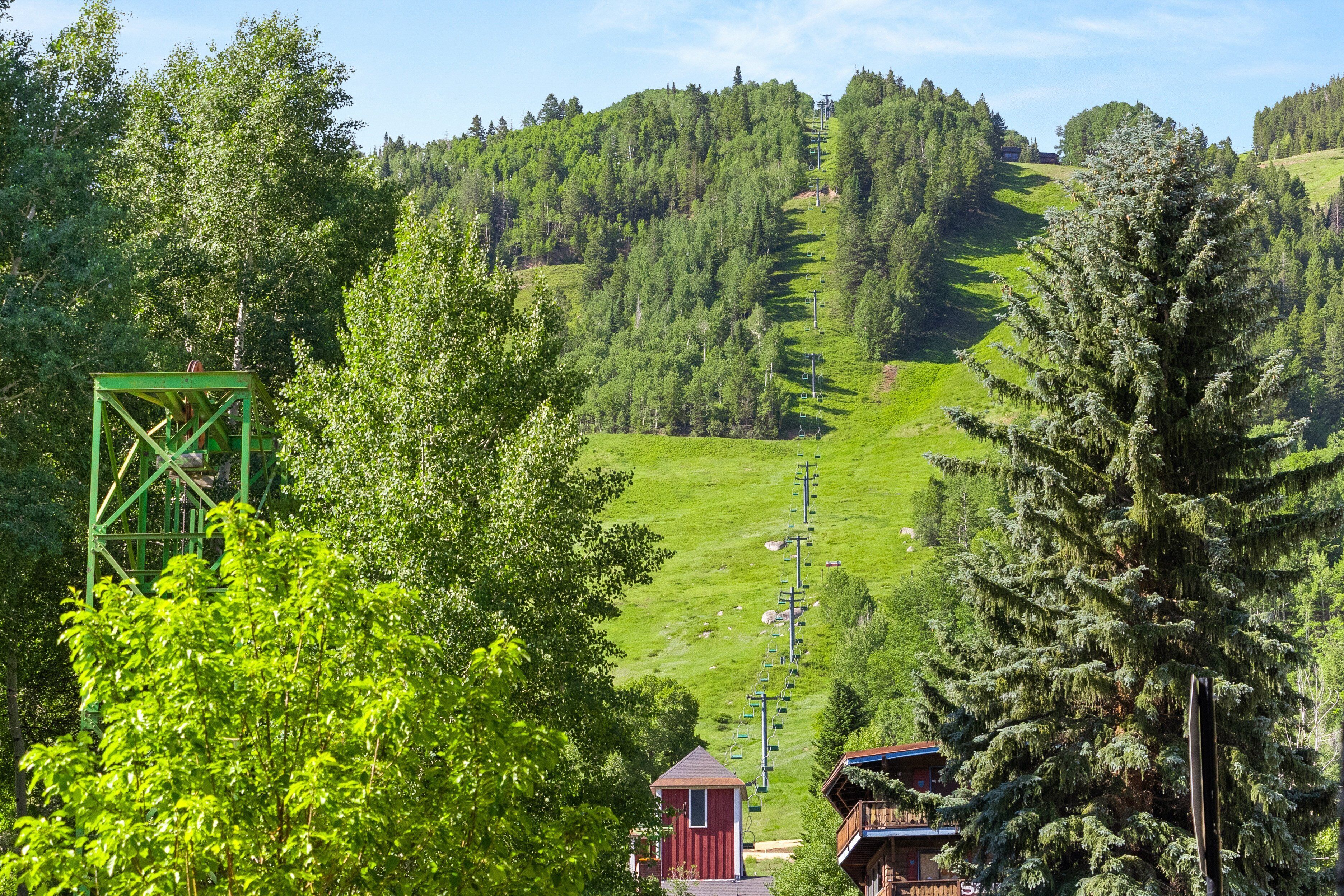 Un paysage montagneux avec un télésiège, des arbres et un petit bâtiment rouge.
