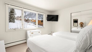 A bedroom with two beds, a TV, a dresser, and a window with a snowy view. - Southpoint 2D | Prime Access to Aspen Mountain, 2 BED / 2 BATH with Stunning Mountain Views (Aspen)