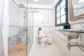 Un baño con cabina de ducha de vidrio, inodoro, lavamanos de vidrio y espejo sobre el lavamanos.