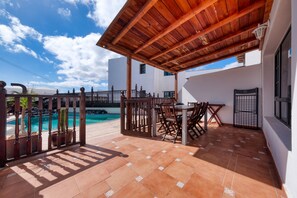 Un patio cubierto con piscina, muebles de madera y vista a la piscina.