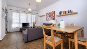 Een woonkamer met een bank, een eettafel met stoelen, een televisie en een boekenkast.