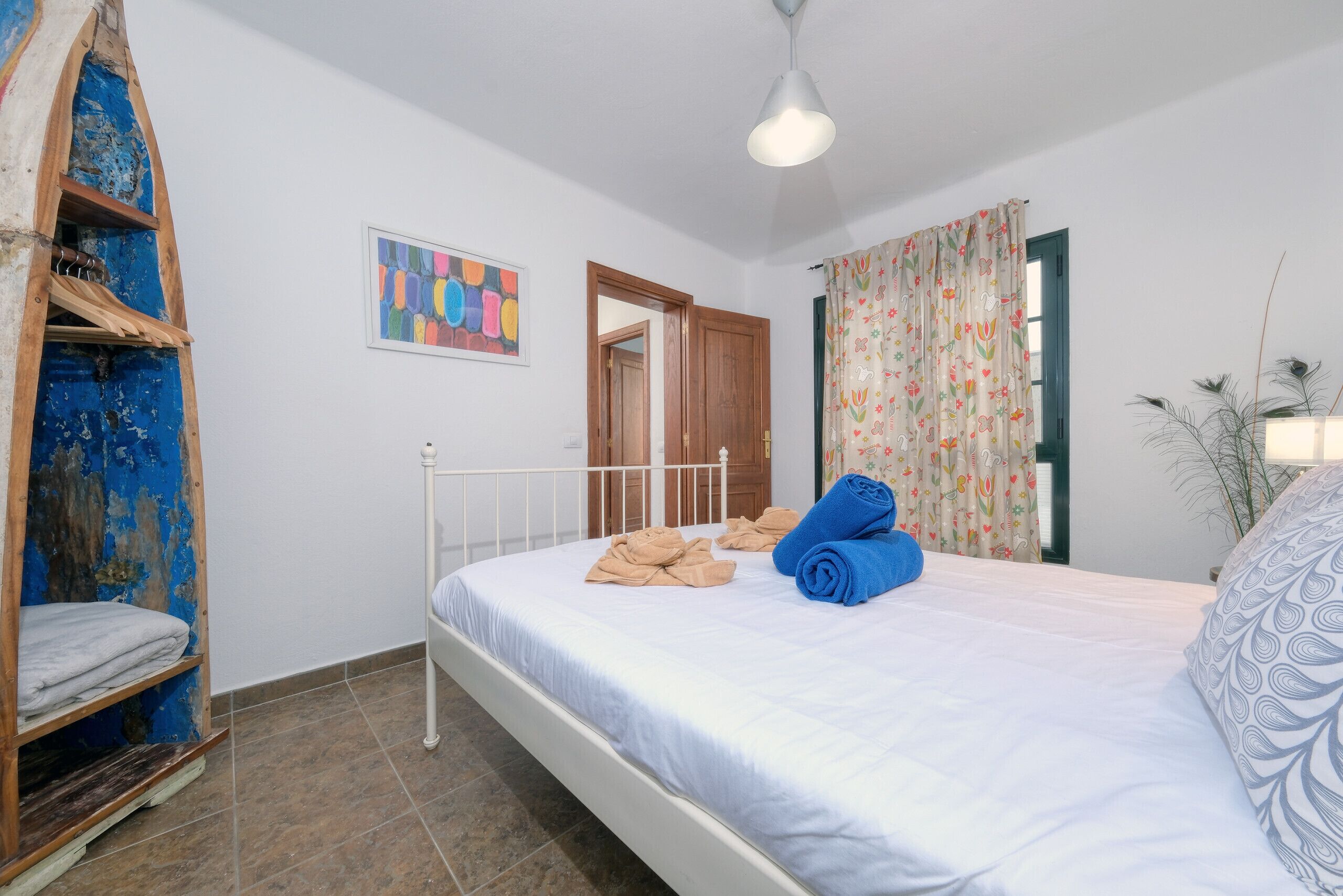 A bedroom with a bed, a wooden shelf unit, a door, and a window with curtains.