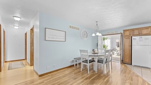 A spacious kitchen with wooden cabinets, a dining area with a white table and chairs, and a hallway with wooden flooring and a rug.