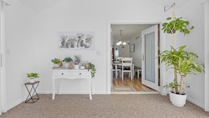 A room with a white desk, a small side table with a plant, a hanging plant, and a door leading to another room.