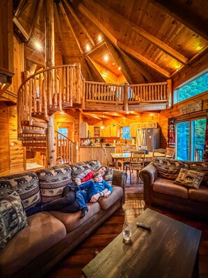 L’intérieur chaleureux d’un chalet avec un escalier en bois, un coin repas et un salon doté de deux canapés.