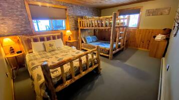 Ein blockhausähnliches Zimmer mit einem Holzbett, Etagenbetten und einer Steinwand.