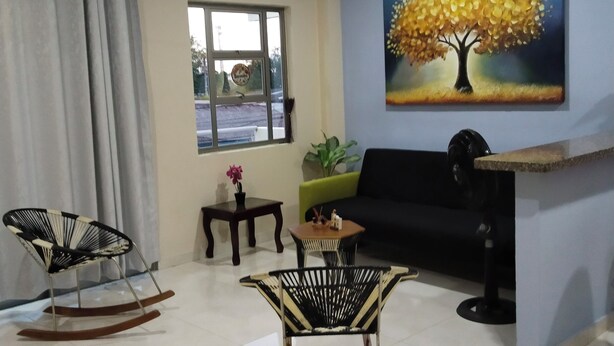 A living room with a ceiling fan, a painting of a tree, a sofa, two rocking chairs, and a small table with a plant. - Furnished apartment, Excellent location, free parking (Cereté)