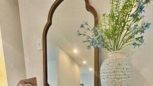 A wooden console table with a mirror, a vase with flowers, and a woven basket underneath. - Short term rental. Home away from your home. (Celina)