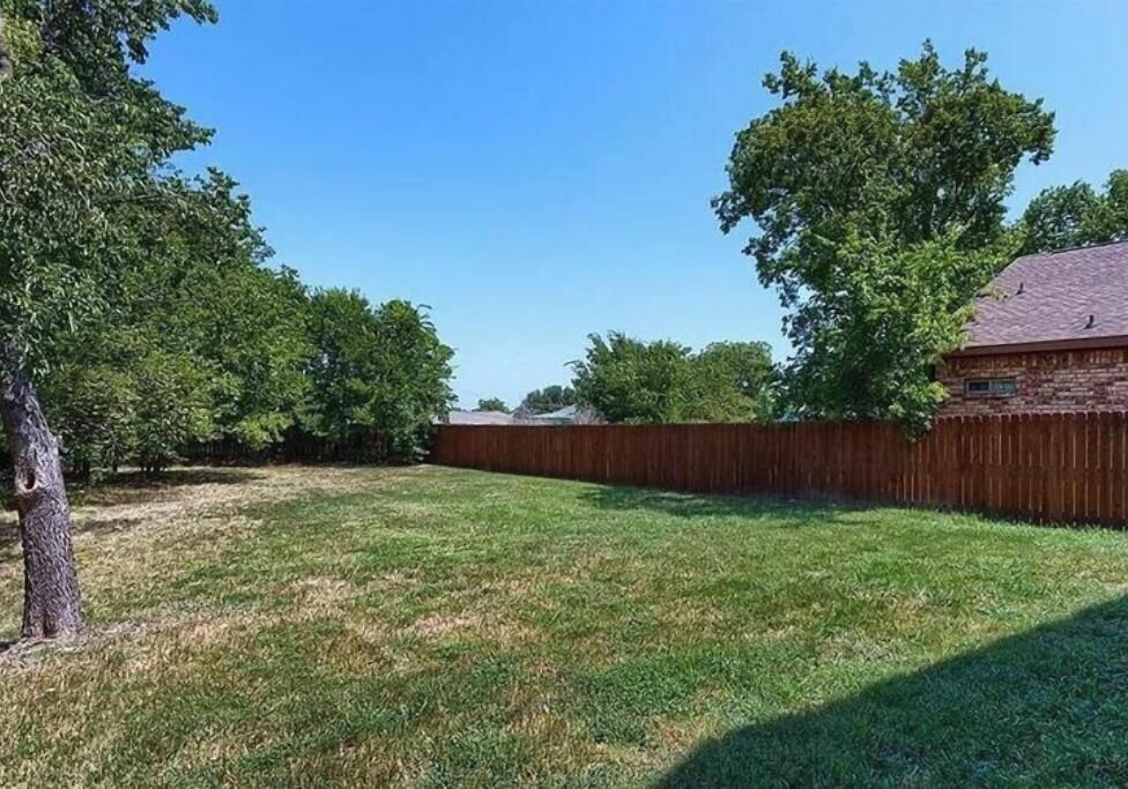 Een achtertuin met een houten omheining, een boom en een huis op de achtergrond.