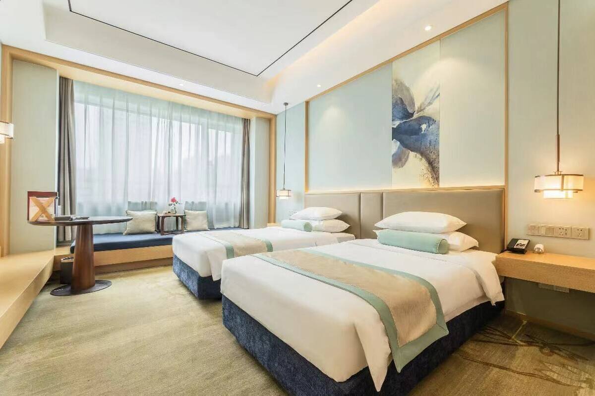 Habitación de hotel con dos camas, un escritorio, un sofá y un ventanal con cortinas.