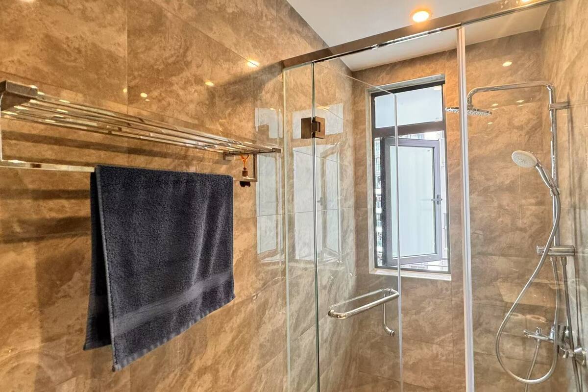 A modern bathroom with a glass shower enclosure, a towel rack with a dark towel, and a window providing natural light.
